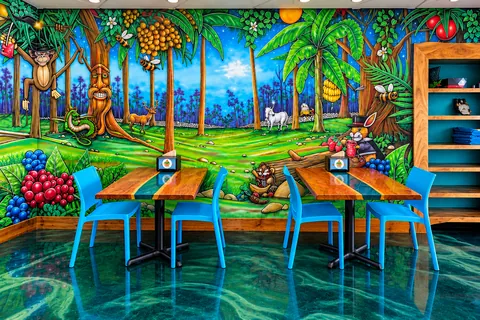 Blue chairs and wooden tables in front of a painted mural of a forest with animals